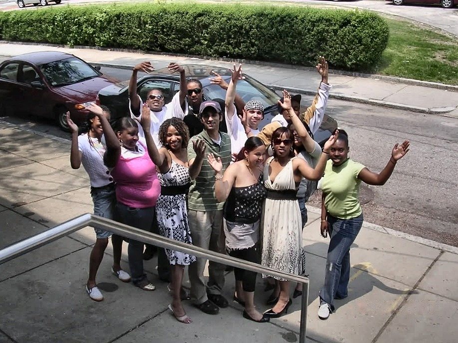 A class of the Excel High School Diploma Program waving on the sidewalk in front of the school